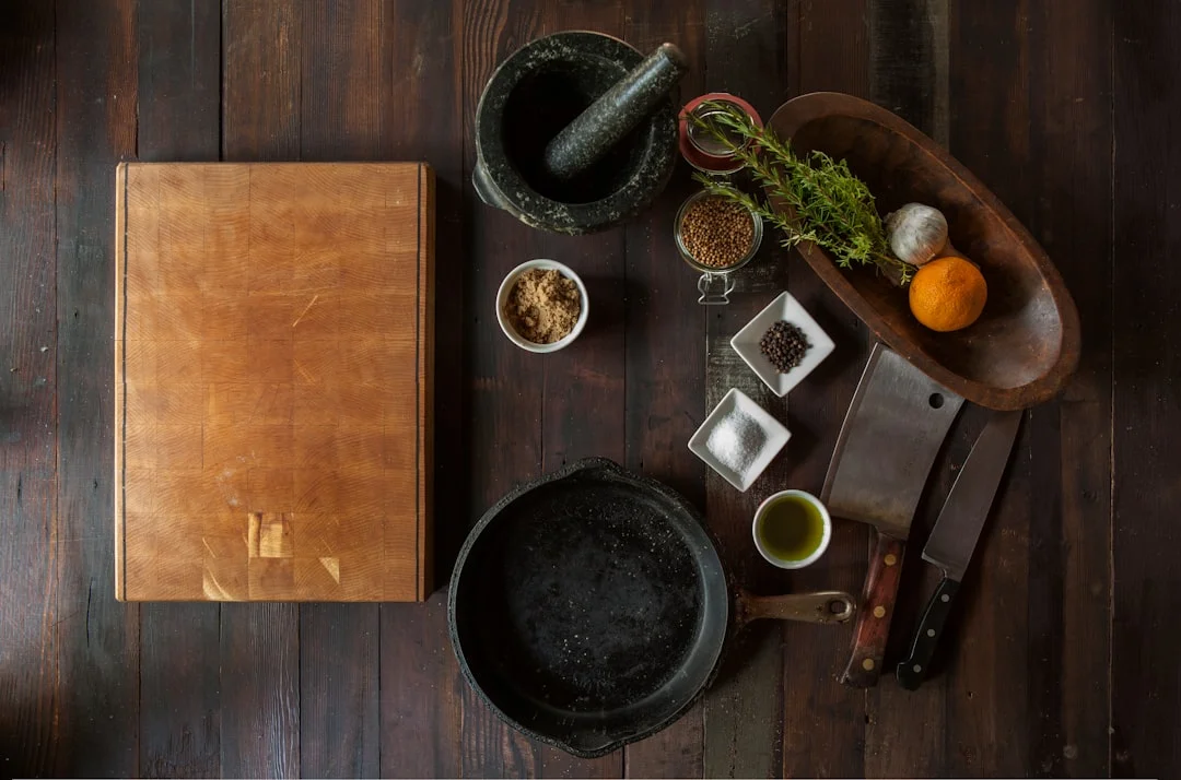 A serious home cook examining a carbon steel skillet on a gas burner, a Japanese chef knife and a whetstone resting on a wooden cutting board nearby